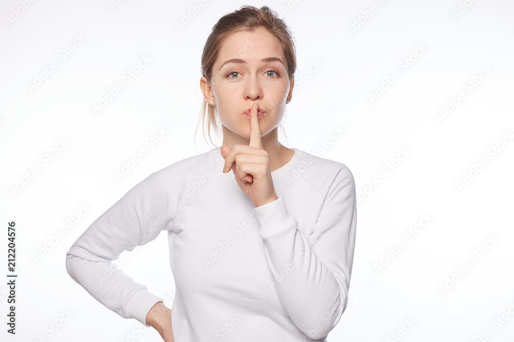 Keep our little secret. Feminine tender Caucasian woman with hair bun, saying shh while showing shush gesture with index finger over mouth, being mysterious or asking silence, telling keep voice down. Keep our little secret. Feminine tender Caucasian woman with hair bun, saying shh while showing shush gesture with index finger over mouth, being mysterious or asking silence, telling keep voice down.