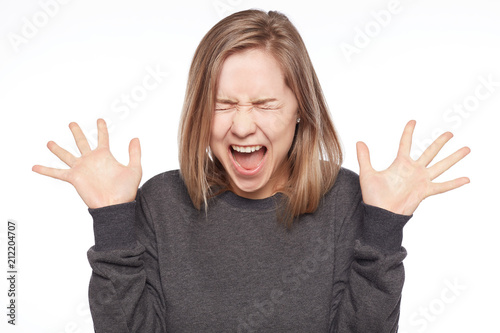 Annoyed female gestures angrily and shouts in annoyance, being discontent with harvest, dressed in casual grey bomber, poses against white studio wall background. Human emotions, irritation concept.