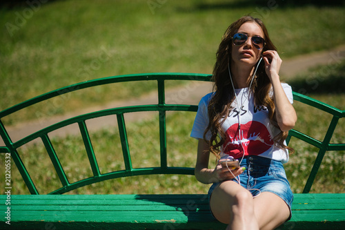 Young beautiful girl listening to music in headphones, sitting on a bench © Vladimir