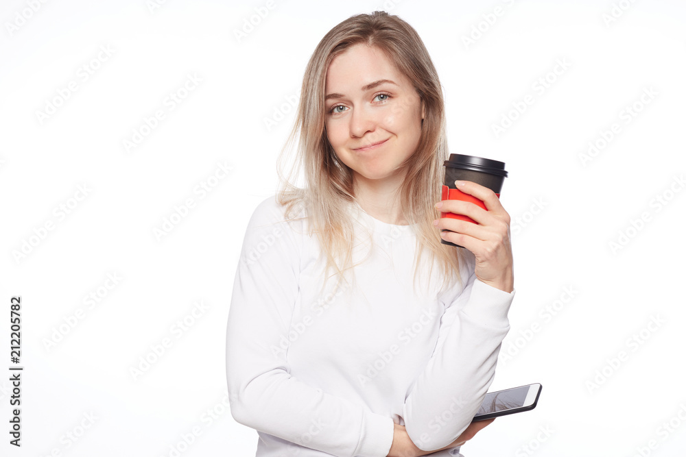Great day to be productive. Good-looking feminine female in shirt and long hairstyle, looking at camerat with sensual smile, holding cup of coffee, having break during lunch at work over white wall. Great day to be productive. Good-looking feminine female in shirt and long hairstyle, looking at camerat with sensual smile, holding cup of coffee, having break during lunch at work over white wall.