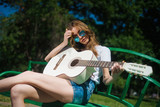 Beautiful young hipster girl playing guitar outdoors in the Park