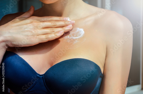 Woman applying moisturizing cream on chest