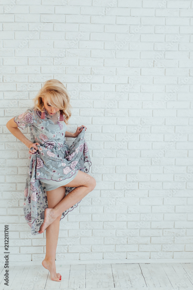 Blonde happy woman in light dress with stay in front of light wall Blonde happy woman in light dress with stay in front of light wall
