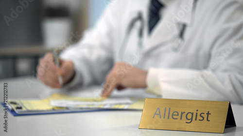 Male allergist completing medical document on laptop, consulting patient online photo