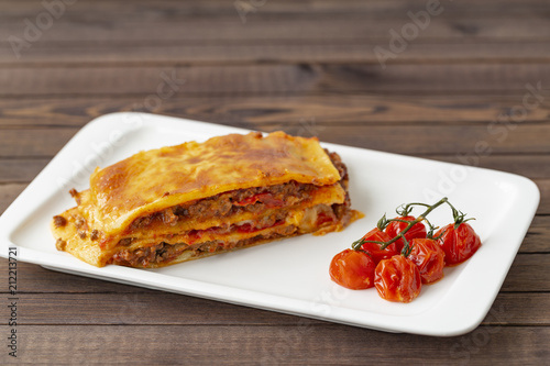 Tasty lasagna with meat covered with cheese, served with baked tomatoes on a white plate.