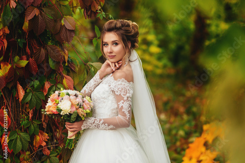 Charming bride with bouquet of flowers stands in a mystic forest
