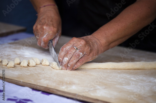 The hands of an elderly woman cut the dough into small pieces. Making Donuts