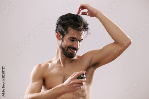 Young man is applying antiperspirant to his armpit. 