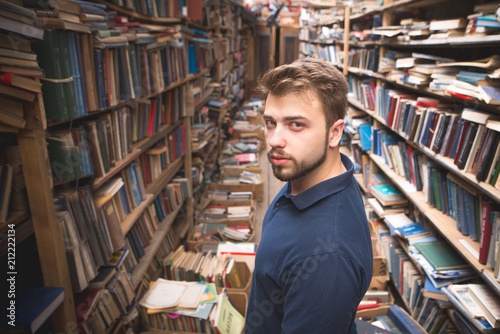 Portrait of a man with a beard standing on the background of an atmospheric public library and looking into the camera. Student in a cozy library.