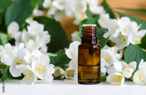 Small bottle of essential jasmine oil. Jasmine blossom flowers background. Copy space. 