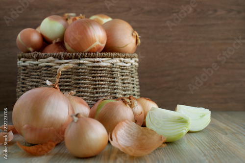 Onions on a wooden background. Onions in a wicker basket. Onion, onion peel, peeled bulbs on a wooden background. Many onions. Vegetables for a healthy diet.