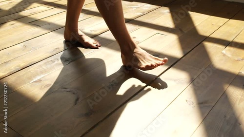 The girl walks on the wooden floor, feet in the sunlight.