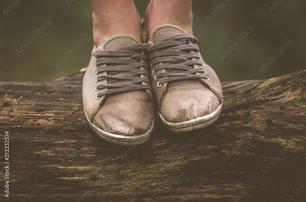 Female legs in gray, worn sneakers on a log