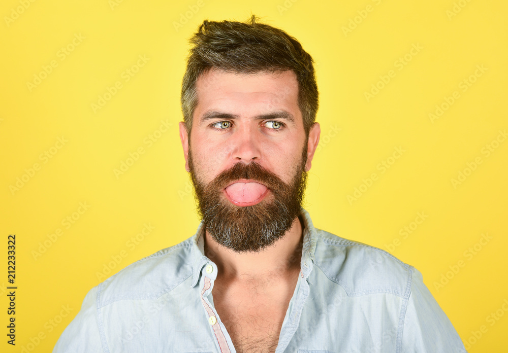 Obraz premium Funny bearded man. Man with beard and mustache. Bearded man shows tongue. Feeling and emotions. Closeup portrait of funny bearded man. Emotions. Feelings. Facial expressions concept. Yellow background