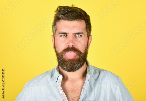 Funny bearded man. Man with beard and mustache. Bearded man shows tongue. Feeling and emotions. Closeup portrait of funny bearded man. Emotions. Feelings. Facial expressions concept. Yellow background
