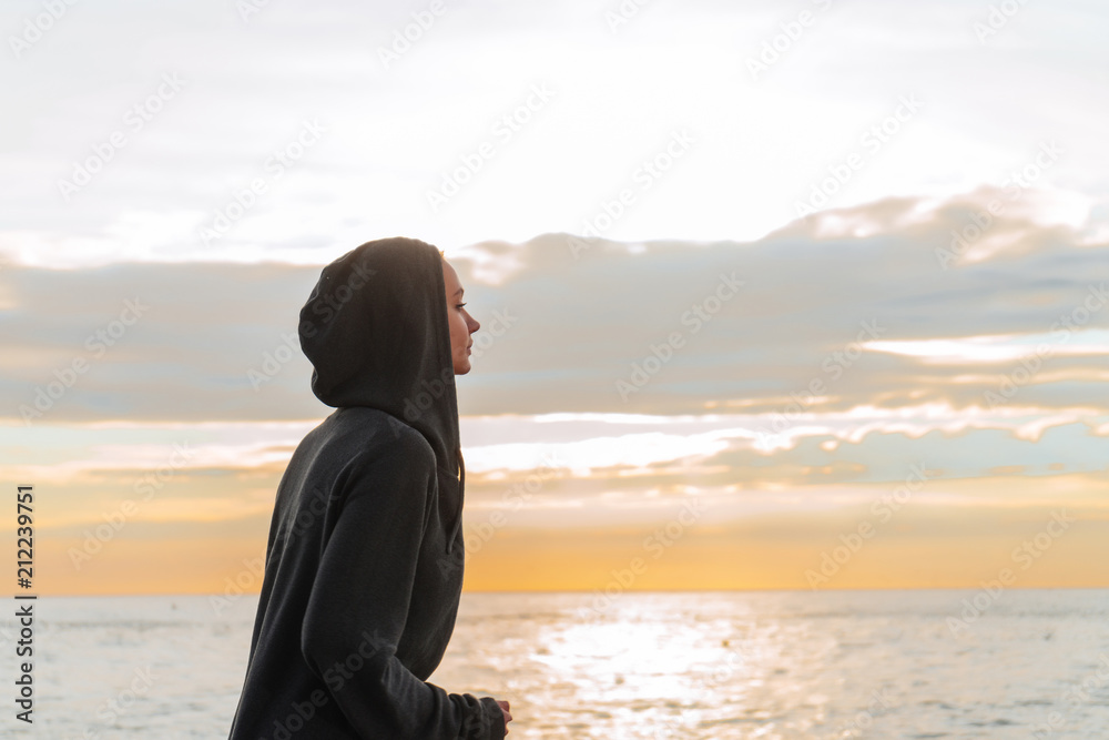 a young girl in a hood is engaged in jogging at sunset on the sea promenade, wants to lose weight