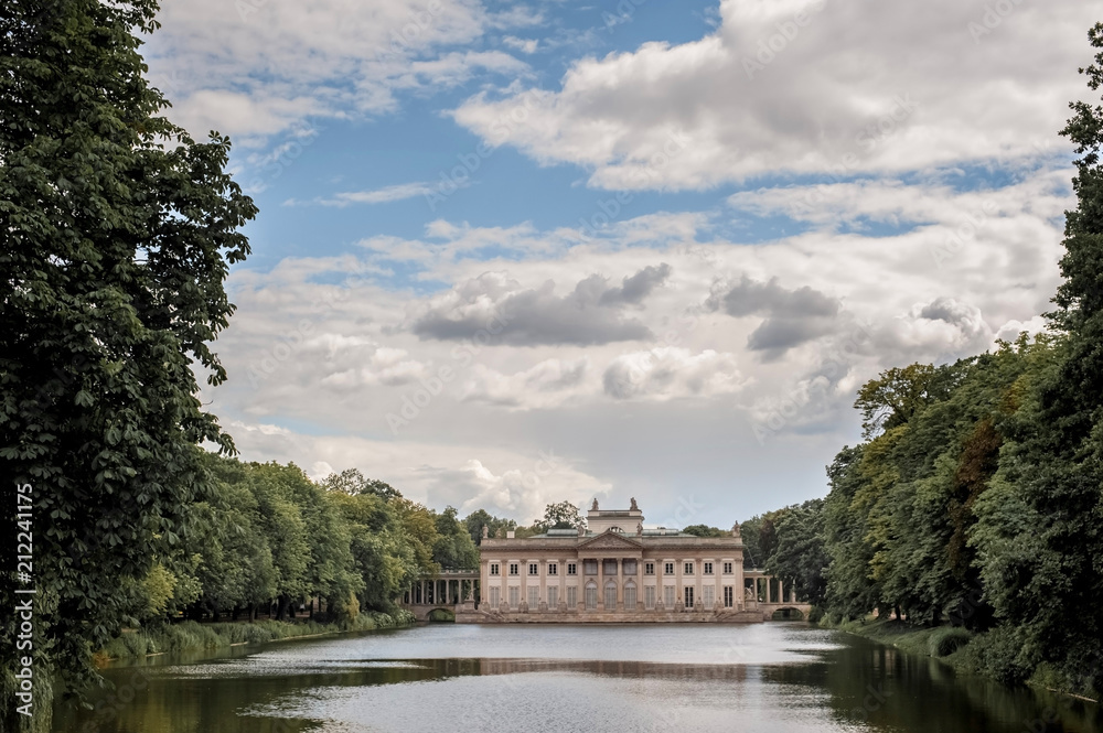 a beautiful architectural building next to the lake in the park; The Palace of Lazenkowski in Poland; Warsaw Historical Park; reflection of architecture in water
