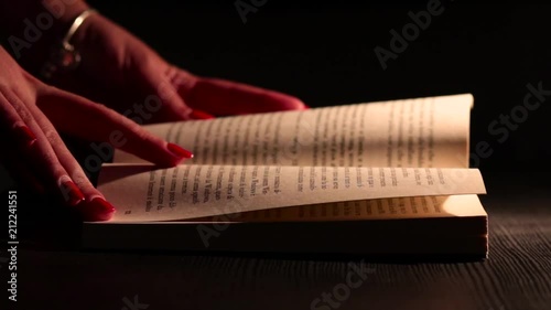 Mano di Donna sfoglia un Libro con Luce Calda. Scena Notturna
