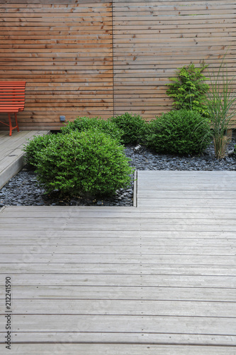 Moderner Gartenbau und Terrassengestaltung: Terrasse aus Holz und Pflanzen im pflegeleichten Schotterbett vor einer Holzwand