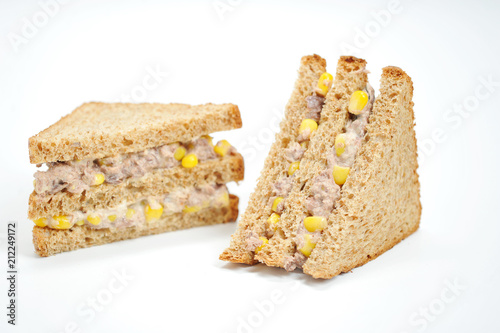 Two sandwiches of a triangular shape on a white background. The filling of the sandwich consists of corn and tuna. Close-up.