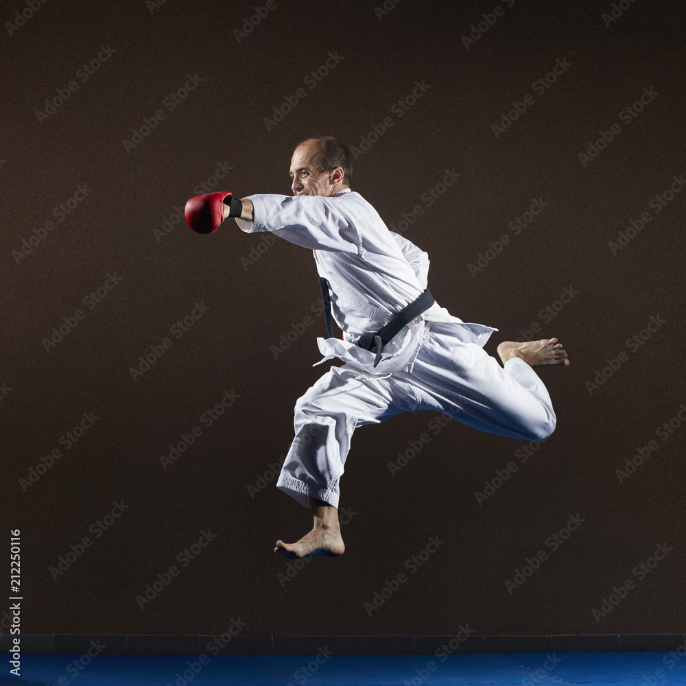 An athlete with red overlays on his hands trains a punch with his hand in a jump