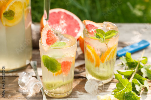 citrus lemonade in glass jug with mint. Orange. Grapefruit and lemon. On greenery background.