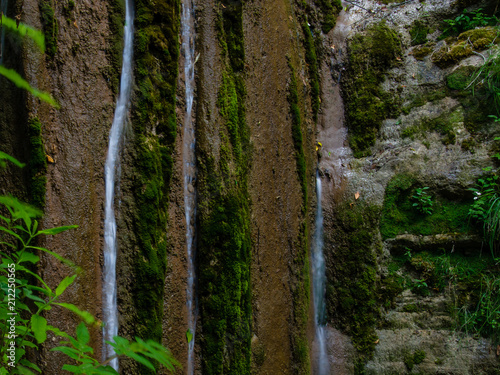 Long exposure small creek waterfall, silver water streams flow down on stones covered with green moss in cold river photo