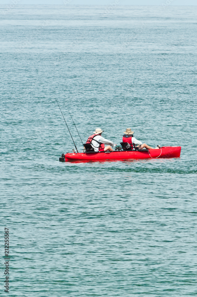Front view, long distance of a young couple fishing from a red, kayak on the calm, tropical waters of the gulf of mexico, on a sunny, summer day
