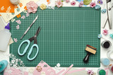 The cutting mat is surrounded by paper flowers, paper, tools and scrapbooking materials. Scrapbooking, top view