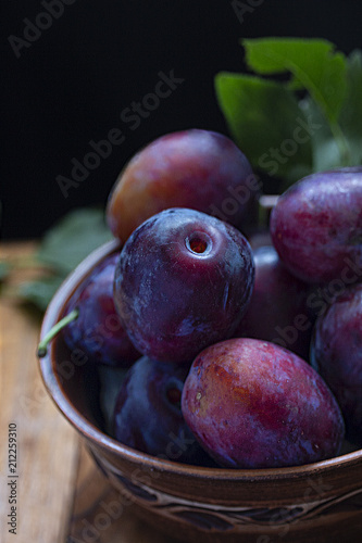 full rural bowl of large ripe colorful blue plums on a wooden table