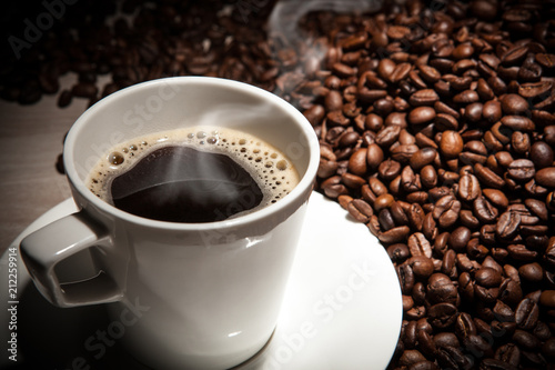 white cup of coffee with steam against a background of fried coffee beans