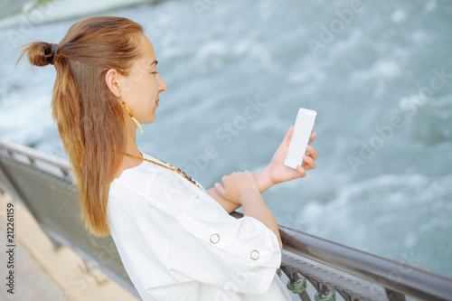 Young woman standing with smartphone on embankment.