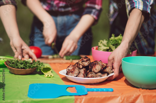 Close up shot of friends cooking together for lunch outdoors. Group of people preparing some food on picnic table outdoors with meat vegetables and herbs.