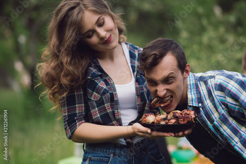 Young man trying to eat piece of chicken from plate of meat. Guy acting silly trying to steal piece of meat from bowl that girl is holding with both of her hands.