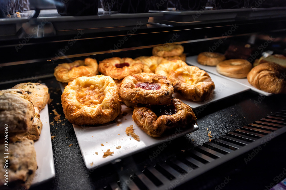 Closeup of many yellow dessert berry fruit baked danish pastries on shelf tray retail display desserts in bakery shop cafe store dark counter Closeup of many yellow dessert berry fruit baked danish pastries on shelf tray retail display desserts in bakery shop cafe store dark counter