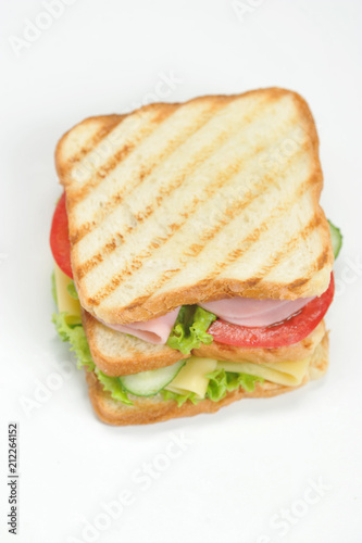 Club-sandwich of white bread. The filling of the sandwich consists of slices of cheese, ham, ripe tomato, fresh cucumber and lettuce leaves. Vertical orientation of the frame. White background.Closeup