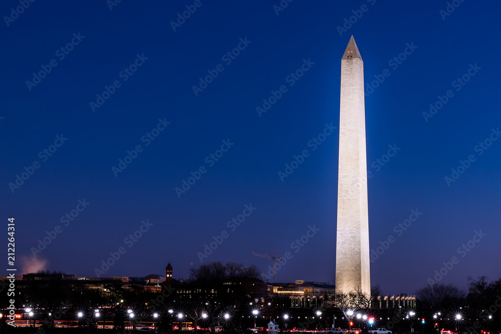 Tall high Washington Monument memorial in blue sky at evening night in winter, lawn, illuminated bright lights dark in December