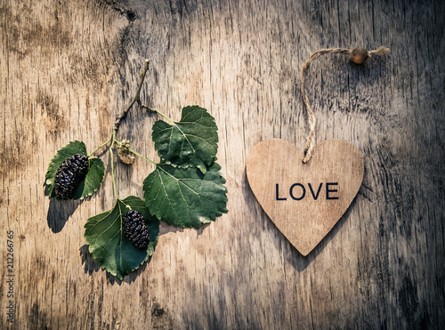 Wooden heart and black berries. A branch of mulberry on a wooden background. Dark background
