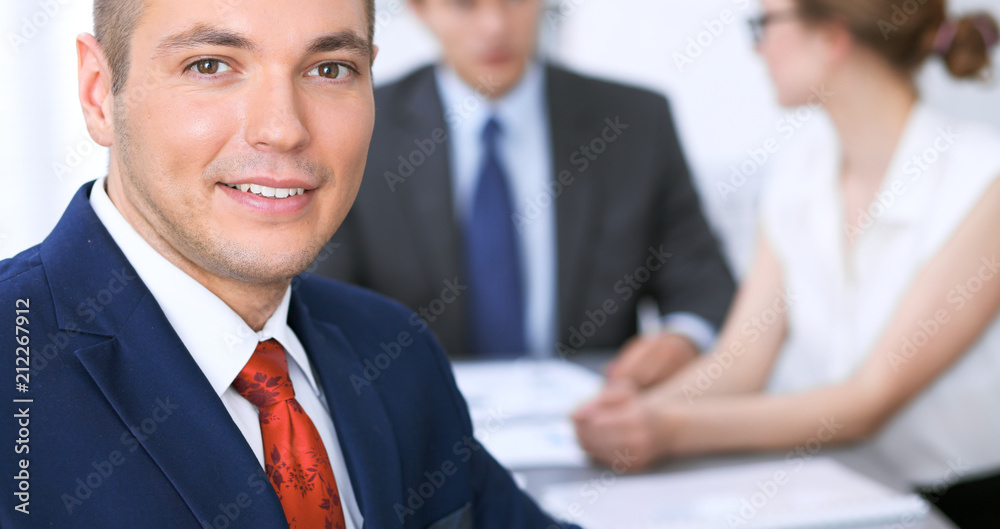 Portrait of cheerful smiling business man against a group of business people at a meeting Portrait of cheerful smiling business man against a group of business people at a meeting