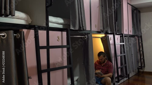 A man is sitting with a ipad in a capsule hotel photo