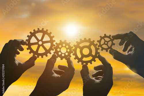 Four hands of businessmen collect gear from the gears of the details of puzzles. against the sunset. The concept of a business idea. Teamwork, strategy, cooperation, innovation.