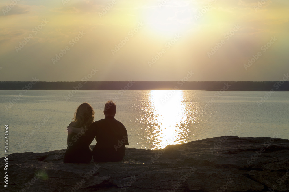 young couple in love sits hugging on the lake shore overlooking the sunset. Happy people.