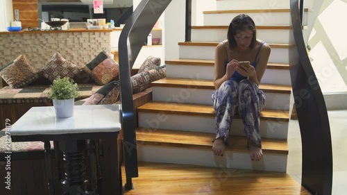 A woman is sitting on the stairs in the house with a smartphone photo