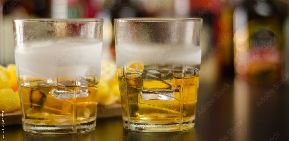glass of whiskey with ice cubes and salty snacks on the background of bottles and bar glass of whiskey with ice cubes and salty snacks on the background of bottles and bar