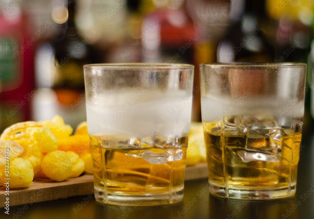 glass of whiskey with ice cubes and salty snacks on the background of bottles and bar glass of whiskey with ice cubes and salty snacks on the background of bottles and bar