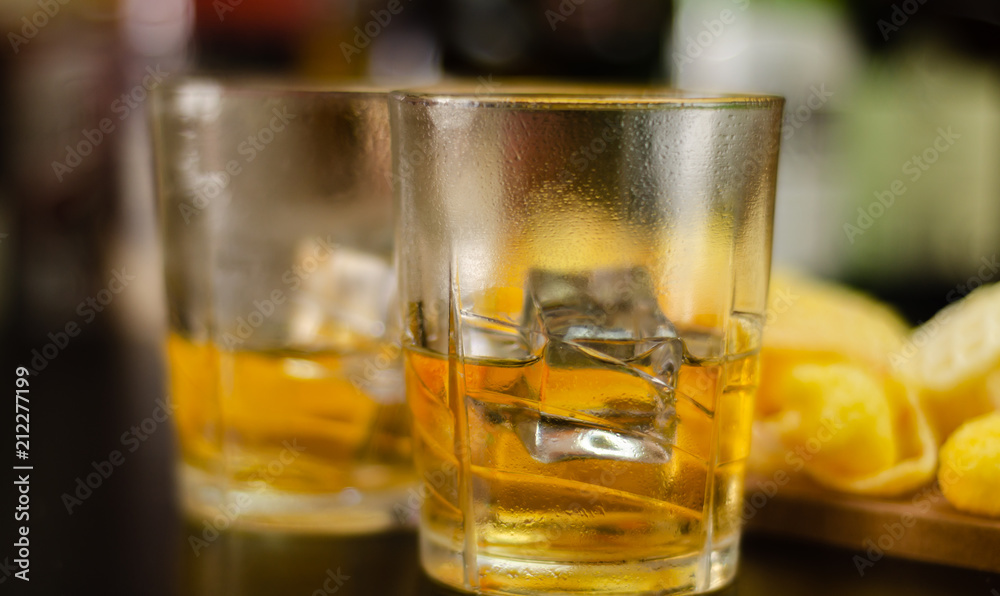 glass of whiskey with ice cubes and salty snacks on the background of bottles and bar glass of whiskey with ice cubes and salty snacks on the background of bottles and bar
