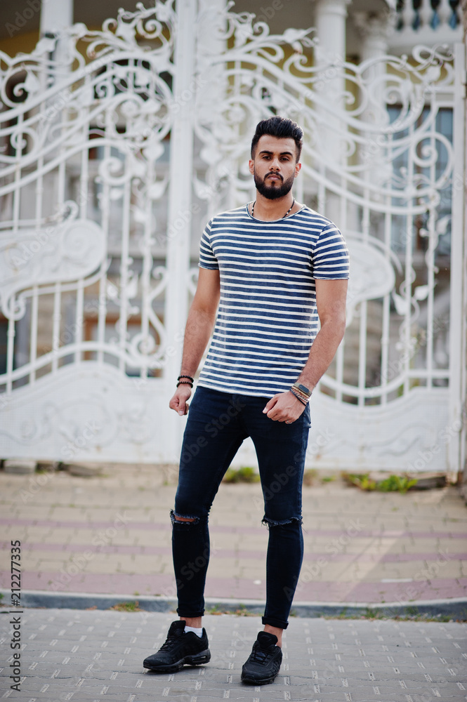 Handsome tall arabian beard man model at stripped shirt posed outdoor against royal iron gates. Fashionable arab guy.