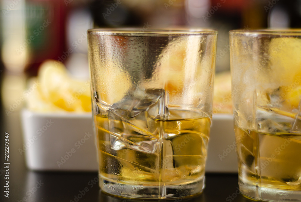 glass of whiskey with ice cubes and salty snacks on the background of bottles and bar glass of whiskey with ice cubes and salty snacks on the background of bottles and bar