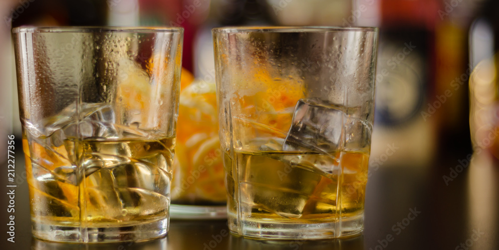 glass of whiskey with ice cubes and salty snacks on the background of bottles and bar glass of whiskey with ice cubes and salty snacks on the background of bottles and bar