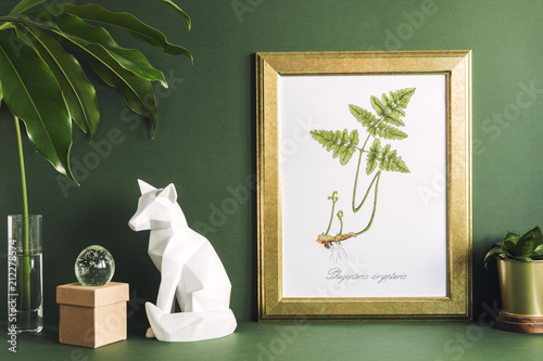 Green modern space with gold mock up poster frame, fox figures, tropical leaf and plant. Stylish desk in green interior. 